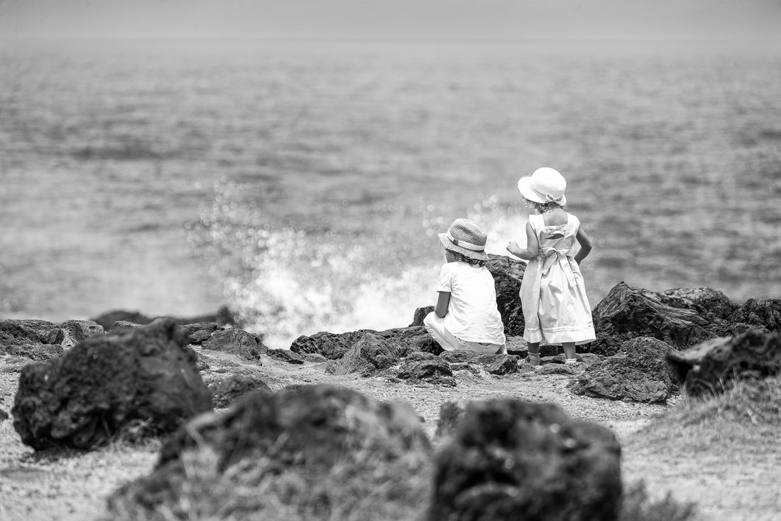 Deux enfants au bord de l'océan, face aux vagues, en noir et blanc